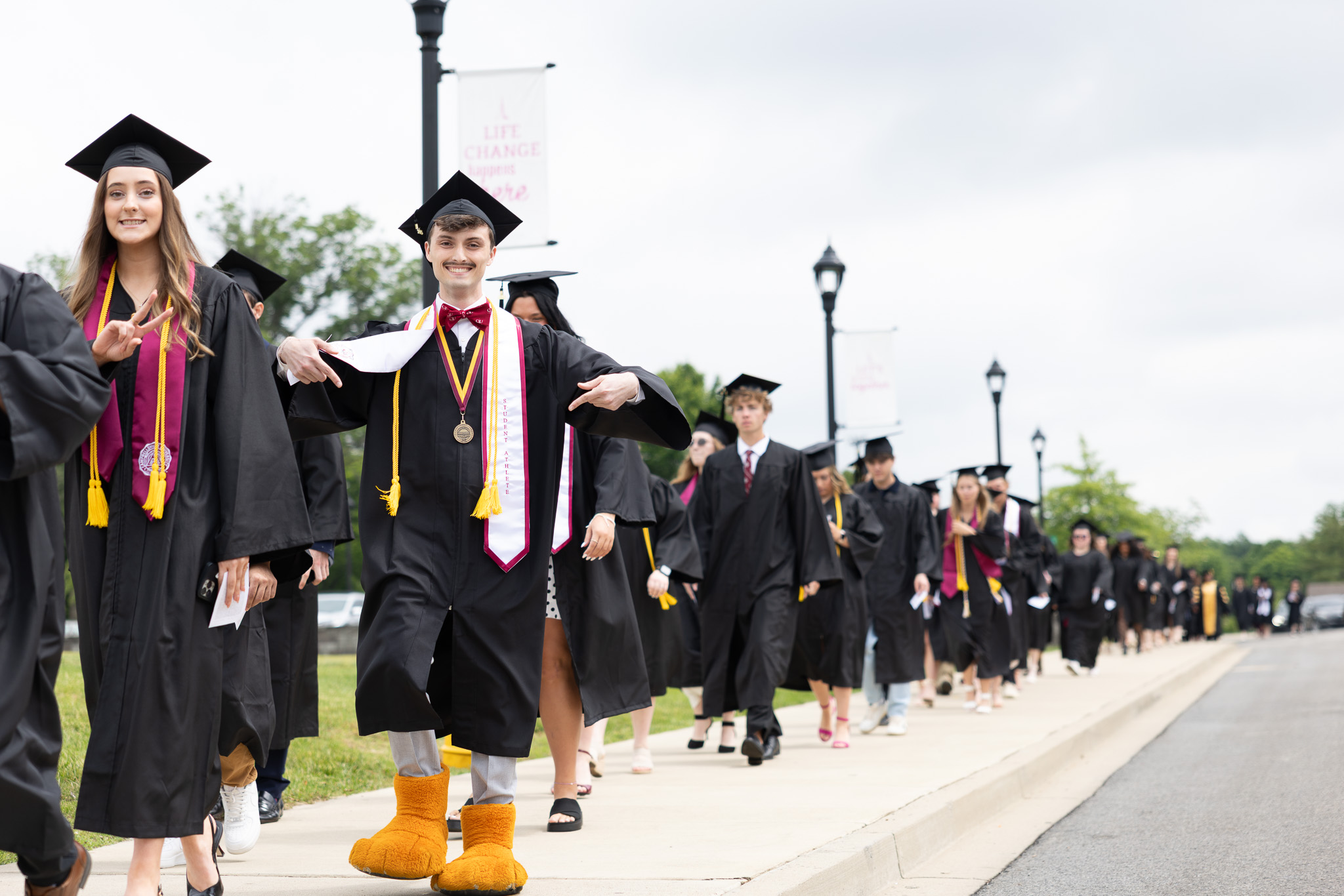 CU Graduate Bryce Osborne takes the graduate’s walk with his classmates and shows off his role as CU mascot Clawz by wearing the recognizable paws