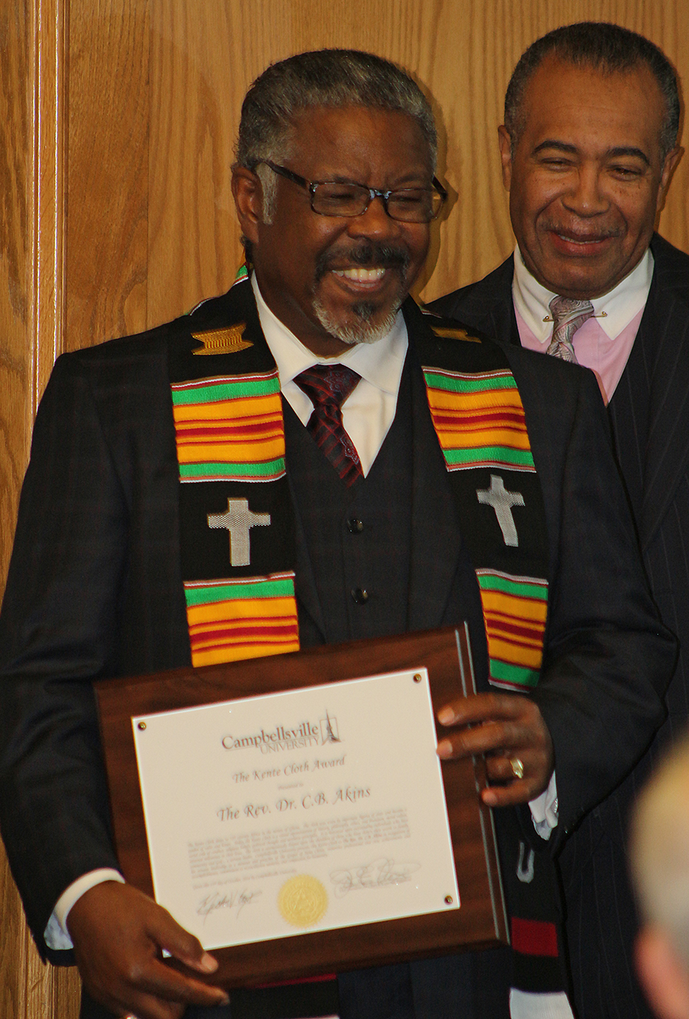 Dr. C.B. Akins, left, upon receiving the Kente  Cloth Award. To the right is Dr. Joseph Owens,  chair of CU’s Board of Trustees, who helped present  the award. (Campbellsville University Photo by  Drew Tucker)