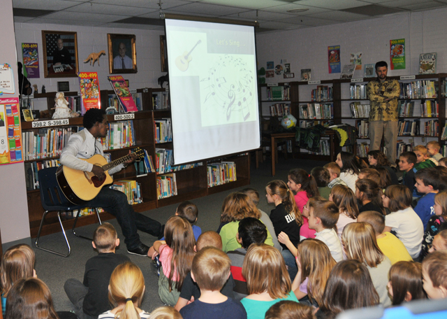 Alpha Rwirangira, left, plays guitar and sings at Taylor County Elementary School. Dr. DeWayne Frazier, right, spoke of his adventures in Rwanda where Rwirangira is from. (Campbellsville University Photo by Elaine Tan)