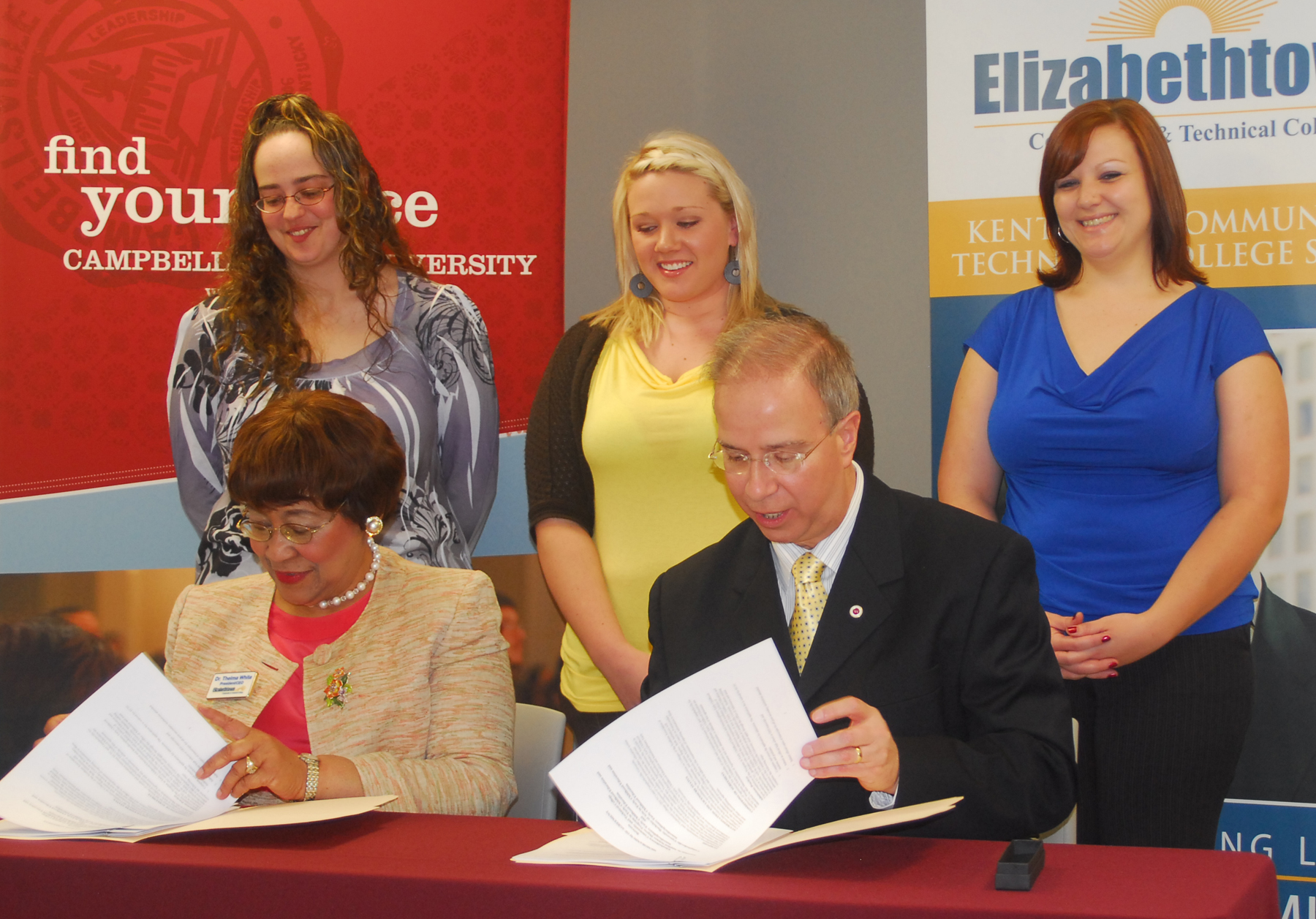 Dr. Michael V. Carter, right, president of Campbellsville University, and Dr. Thelma White, president and chief executive officer of Elizabethtown Community & Technical College, sign memoranda of agreement between their two institutions that will allow ECTC students to transfer credits to CU and obtain four bachelor degrees. Students watching the signing were: from left, Jessica Haire of Elizabethtown, a student at ECTC; and CU students Brooke Cooper of Russell Springs, Ky., and Amanda Adkins Powers of Hodgenville. (Campbellsville University Photo by Joan C. McKinney)