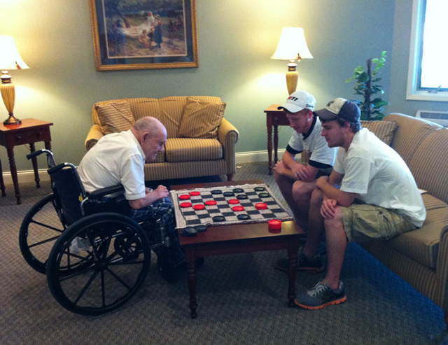 Campbellsville University students Joseph McDonald of Louisville, Ky., left sitting on couch, and Joey Bomia of Fredonia, Ky., right sitting on couch, play checkers with Bob Romines at Grandview Nursing and Rehabilitation Facility as part of a partnership between CU and Grandview to build intergenerational relationships. (Photo