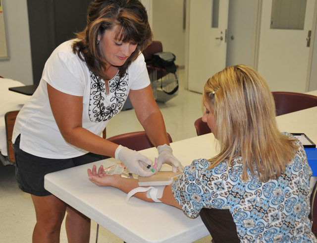 Teresa Dodrill of Columbia, Ky., left, practices drawing blood on Christie Glasscock, RN, the  Campbellsville University Technology Training Center allied health facilitator. (Campbellsville University Photo by Whitney Vaughn)