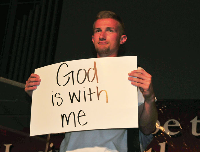 Zach Napier, Campbellsville University sophomore and FCA camp huddle leader, shares a piece of his testimony displayed on poster board, during worship. (Campbellsville University Photo by Josh Christian) 