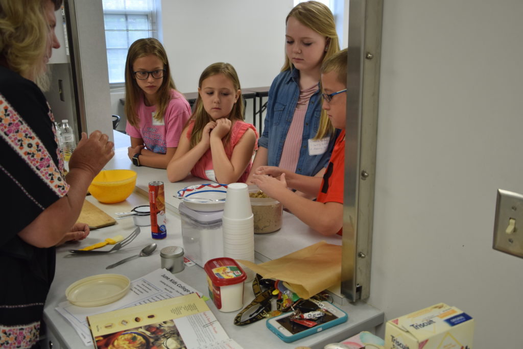 Pam Tennant, left, leads the Kids College Cooking up a Storm class on Campbellsville University’s campus. Tennant shows, from left, Chloe Thompson of Campbellsville, Ky., Emily VanHoosier of Lebanon, Ky., Gabriella VanHoosier of Lebanon, Ky., and Jaxon McCubbin of Campbellsville, Ky. how to measure their ingredients for their recipe of the day. (Campbellsville University Photo by Ariel Emberton)