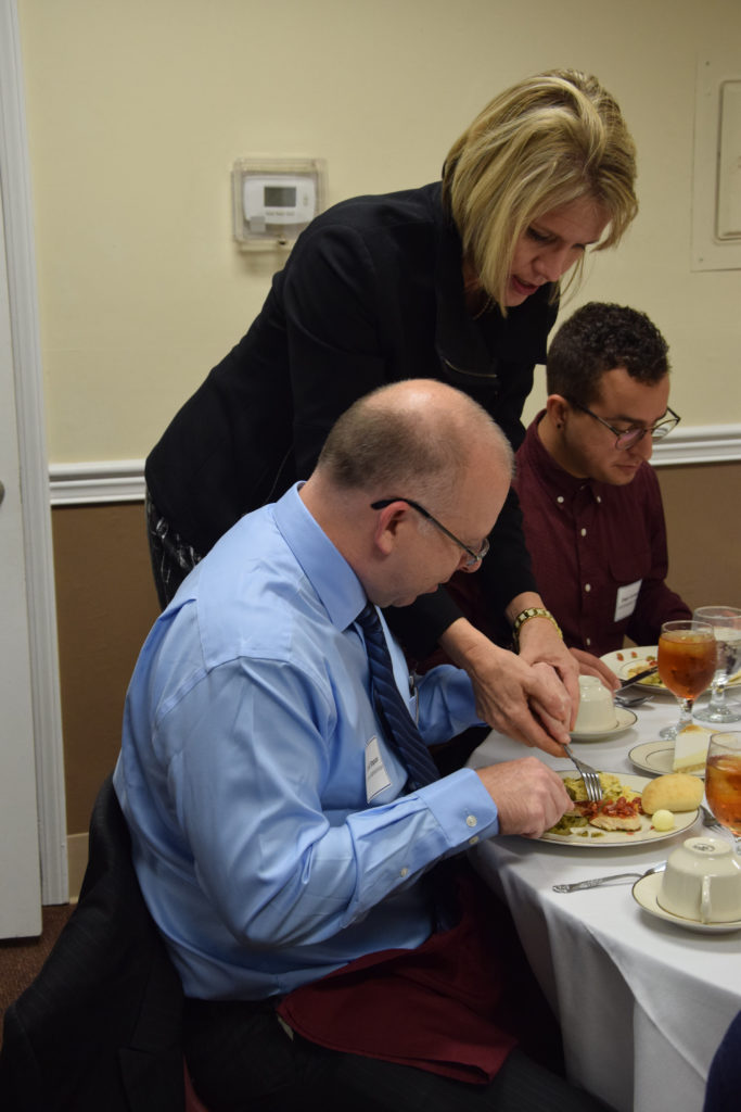 Terri Thompson, shows David Simpson, left, a business administration major from Edmonton, Ky., and Diego Cardenas, a senior art/graphic design student from Venezuela, how to cut their entrée at the dining etiquette dinner. (Campbellsville University Photo by Kasey Ricketts)